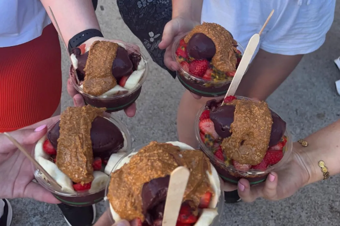 The photo is focused on five female hands holding delicious acai bowls with a variety of toppings